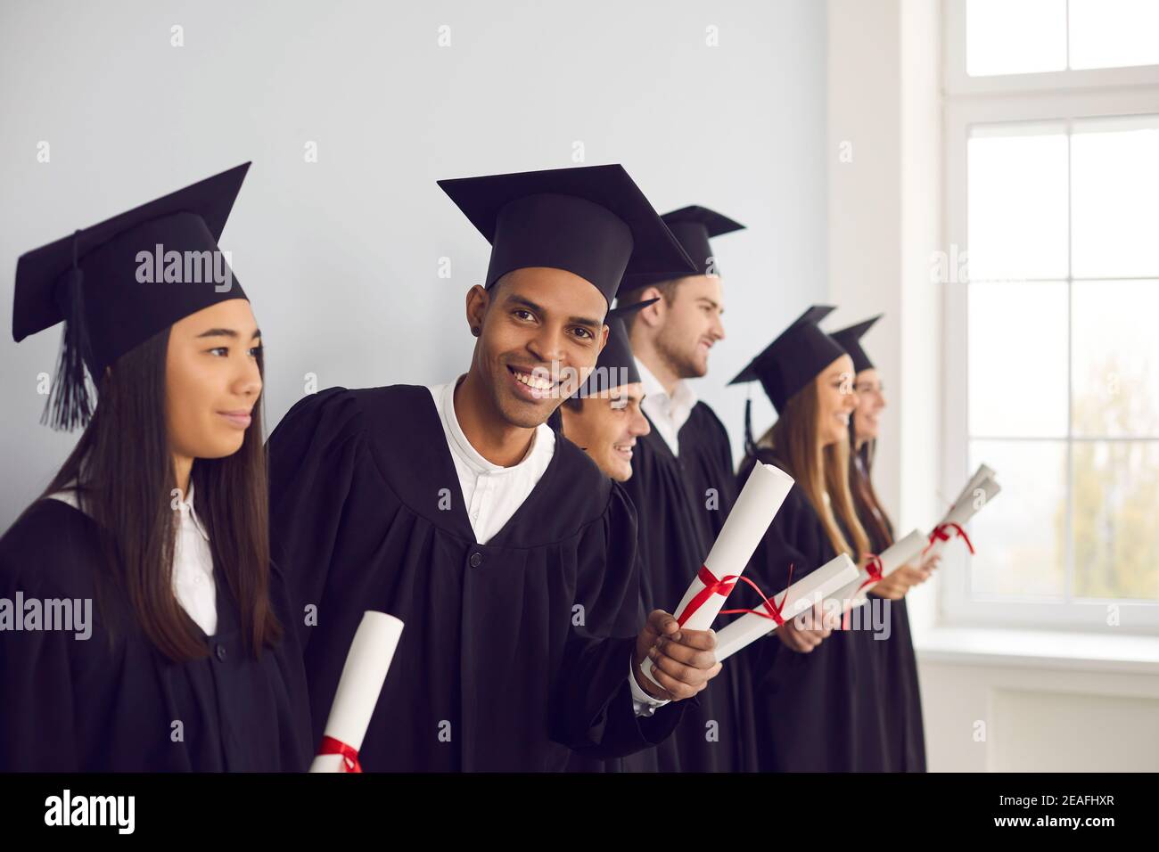 Buon laureato che tiene il diploma e guardando la macchina fotografica, in piedi in fila con altri allievi Foto Stock
