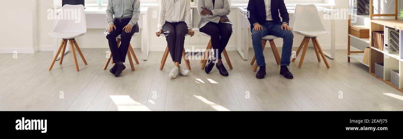 Immagine ritagliata delle gambe di varie persone sedute su sedie e in attesa del loro turno. Foto Stock