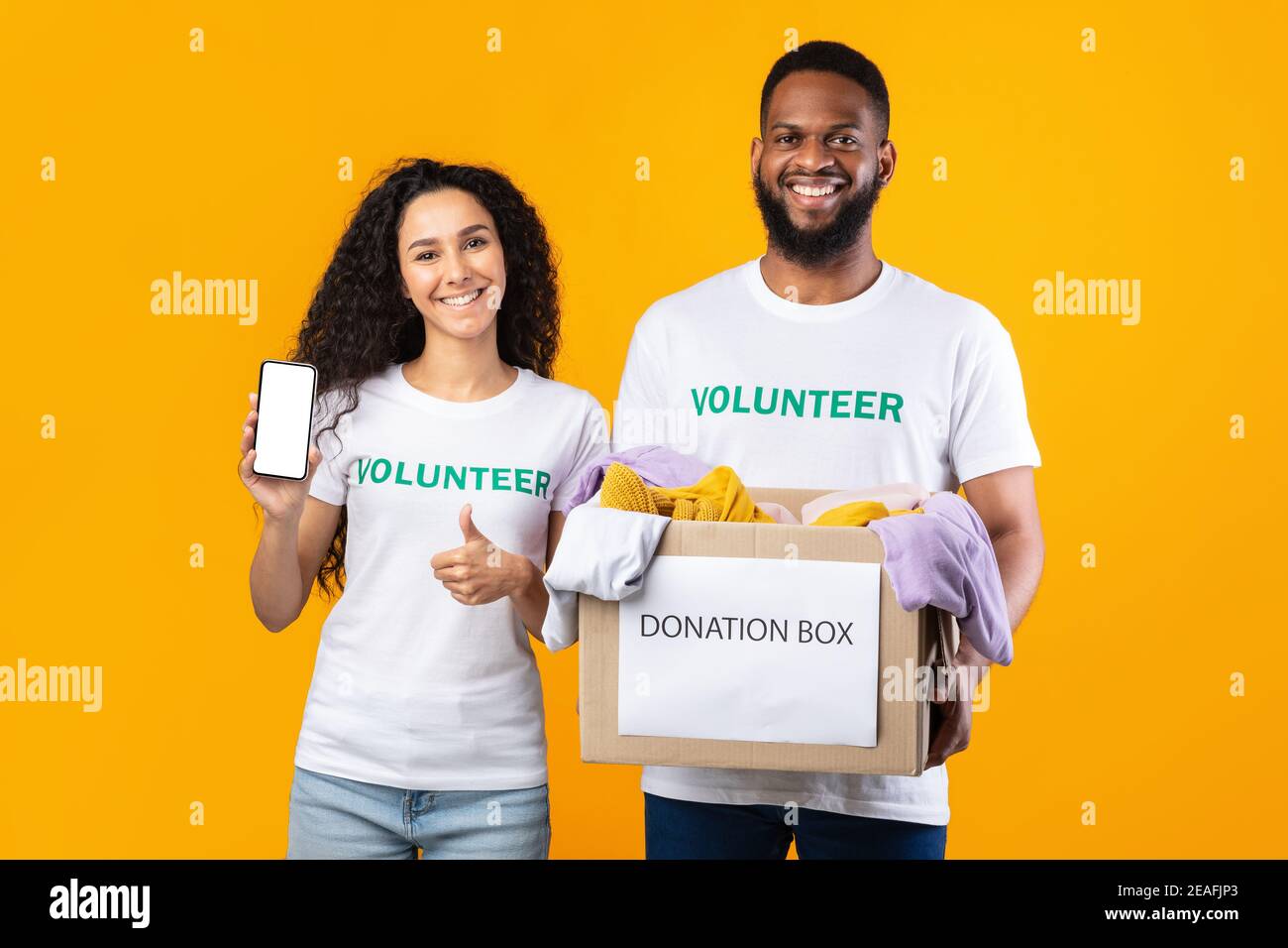 Due volontari che mostrano Telefono schermo Holding Donation Box, sfondo giallo Foto Stock