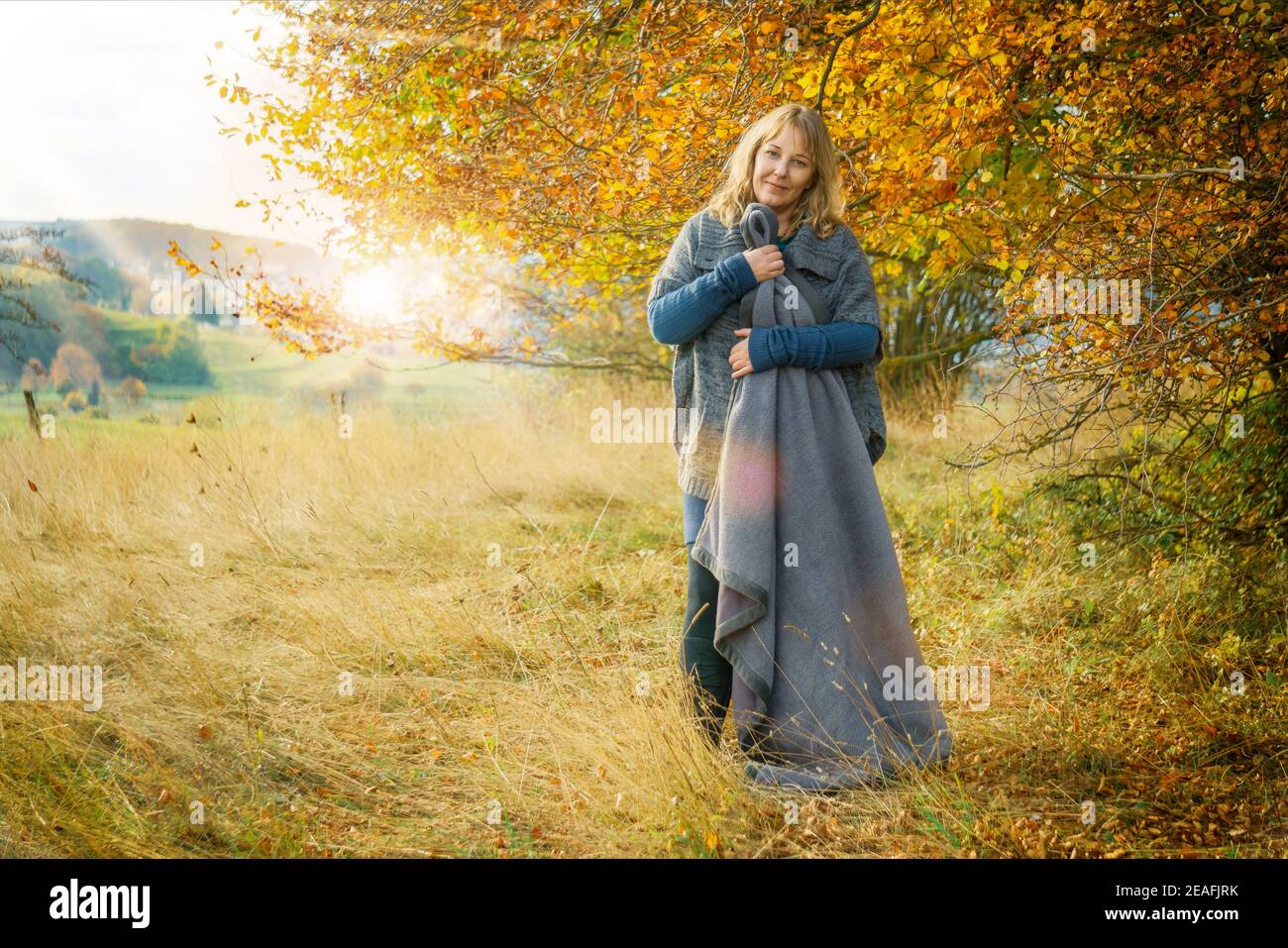 Una donna di 40 anni nel paesaggio naturale autunnale. La donna bionda indossa abiti in lana e stivali. Ha una coperta. Foto Stock