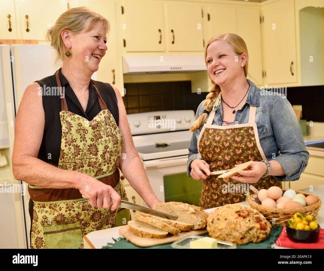 Due belle donne caucasiche in grembiule, affettare pane appena sfornato su banco da cucina, pane macellante, Wisconsin, USA Foto Stock