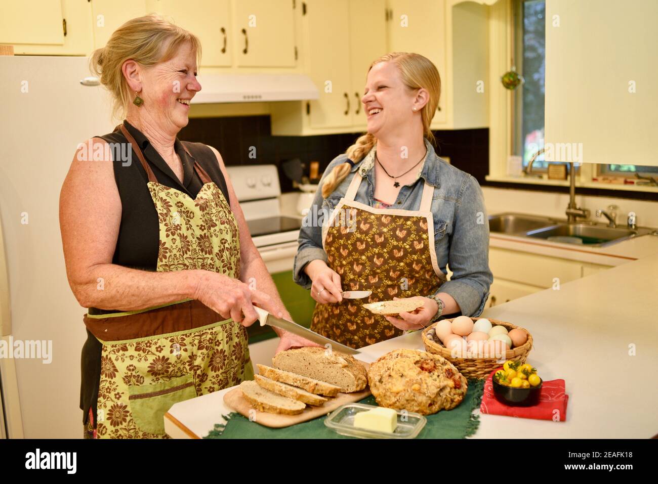 Due belle donne caucasiche in grembiule, affettare pane appena sfornato su banco da cucina, pane macellante, Wisconsin, USA Foto Stock