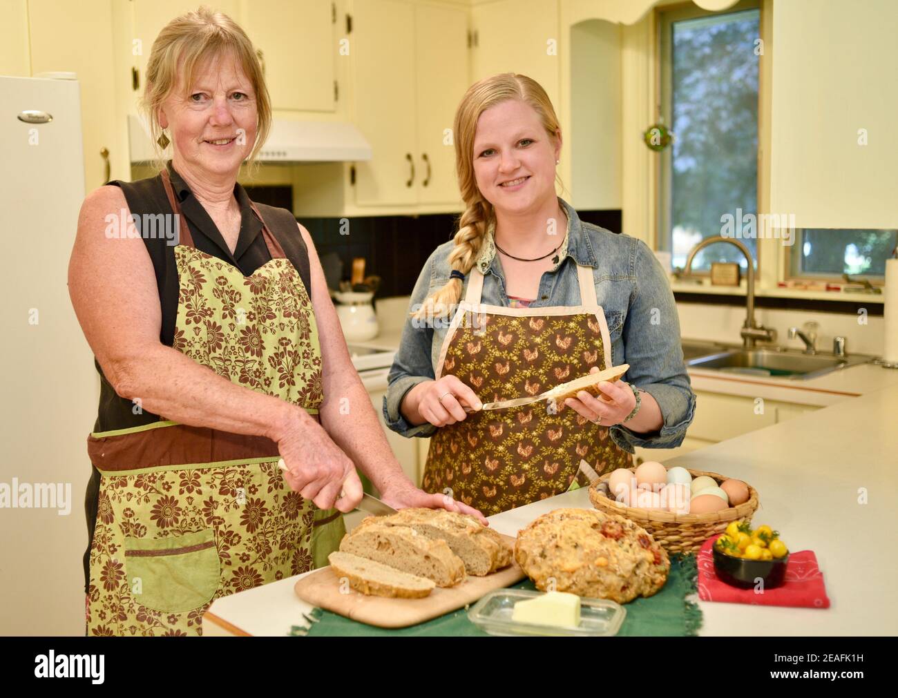 Due belle donne caucasiche in grembiule, affettare pane appena sfornato su banco da cucina, pane macellante, Wisconsin, USA Foto Stock