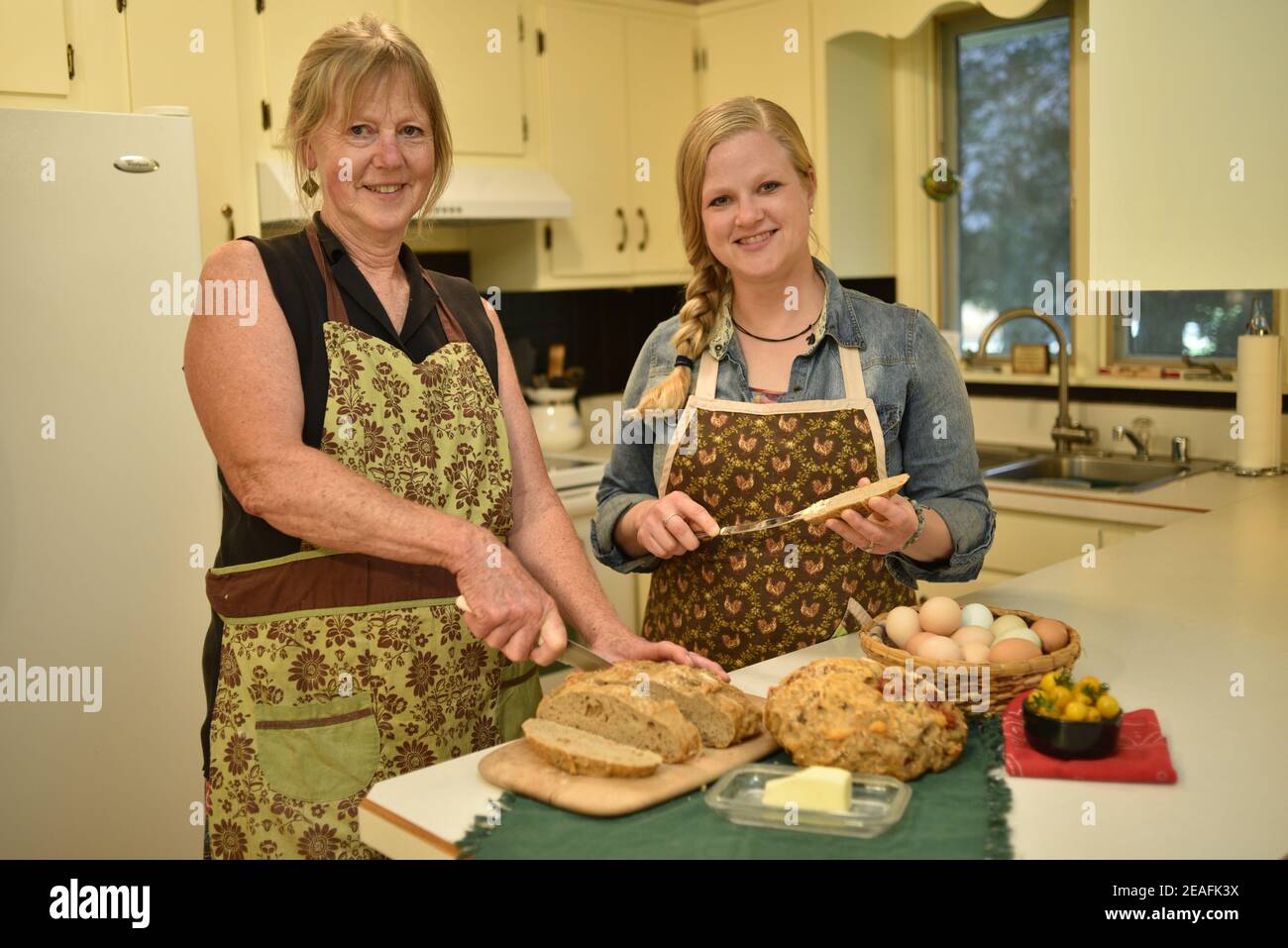 Due belle donne caucasiche in grembiule, affettare pane appena sfornato su banco da cucina, pane macellante, Wisconsin, USA Foto Stock