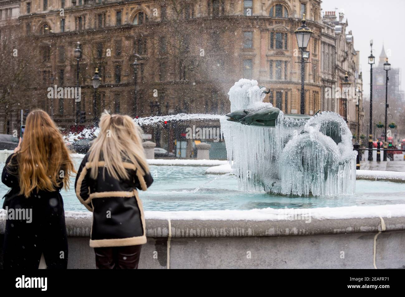 Londra, Regno Unito. 9 febbraio 2021. UK Weather: Le donne visualizzano una fontana ghiacciata coperta di ghiaccio in Trafalgar Square durante le nevi leggere come il freddo tempo portato da Storm Darcy continua. Credit: Stephen Chung / Alamy Live News Foto Stock