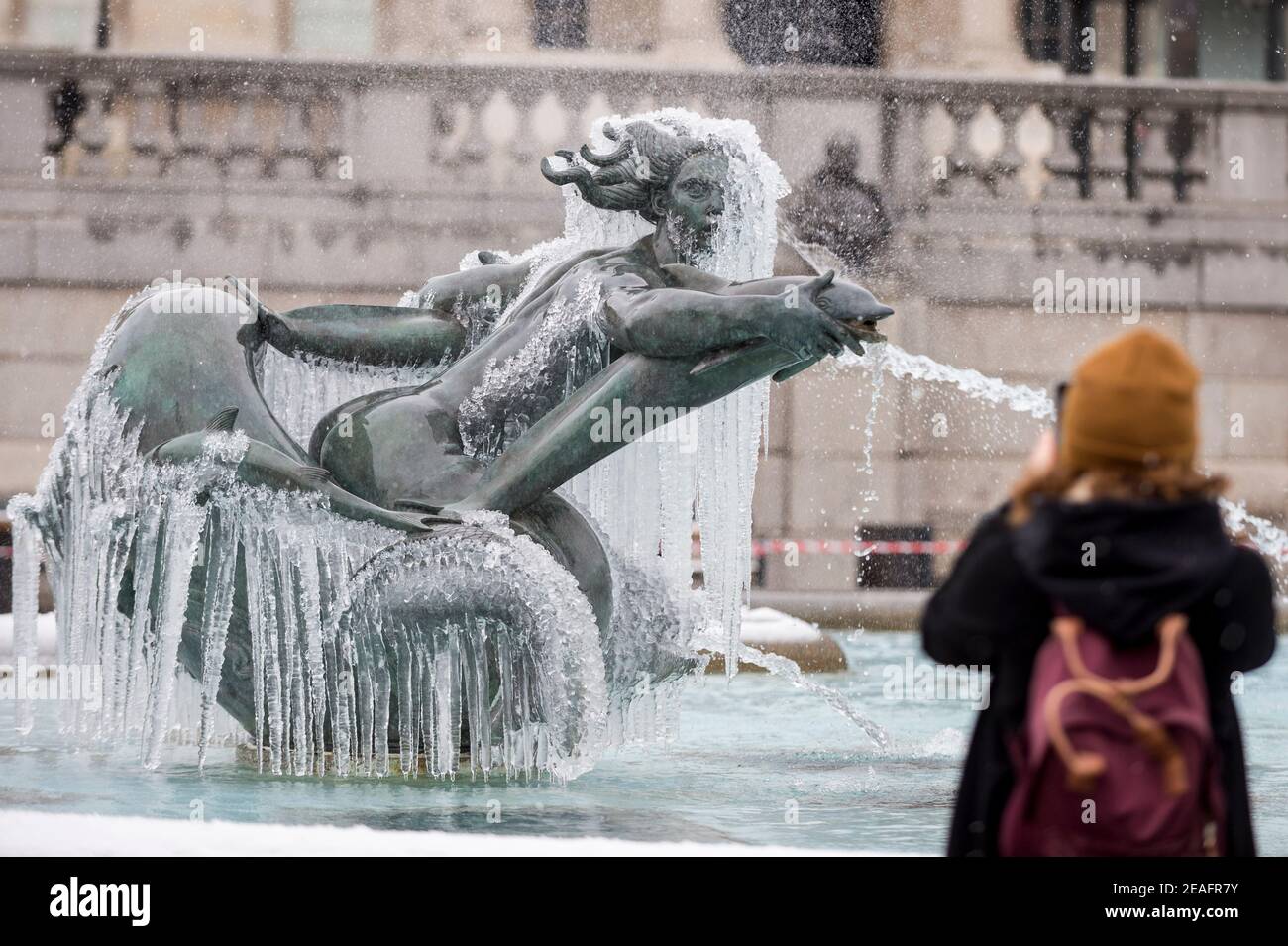 Londra, Regno Unito. 9 febbraio 2021. UK Weather: Una donna vede una fontana ghiacciata coperta di ghiaccio in Trafalgar Square durante le nevi leggere flurries, mentre il clima freddo portato da Storm Darcy continua. Credit: Stephen Chung / Alamy Live News Foto Stock
