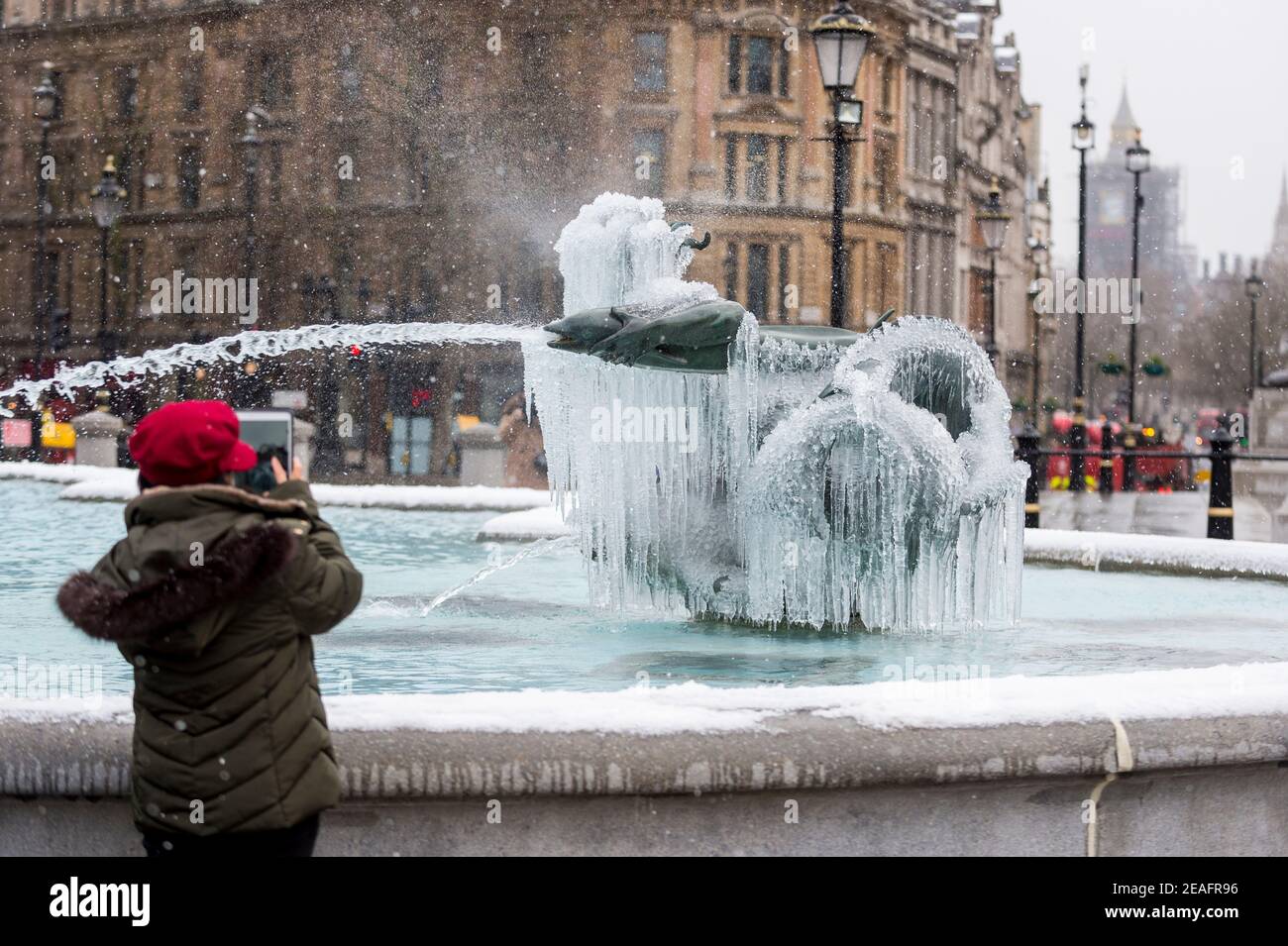 Londra, Regno Unito. 9 febbraio 2021. UK Weather: Una donna vede una fontana ghiacciata coperta di ghiaccio in Trafalgar Square durante le nevi leggere flurries, mentre il clima freddo portato da Storm Darcy continua. Credit: Stephen Chung / Alamy Live News Foto Stock