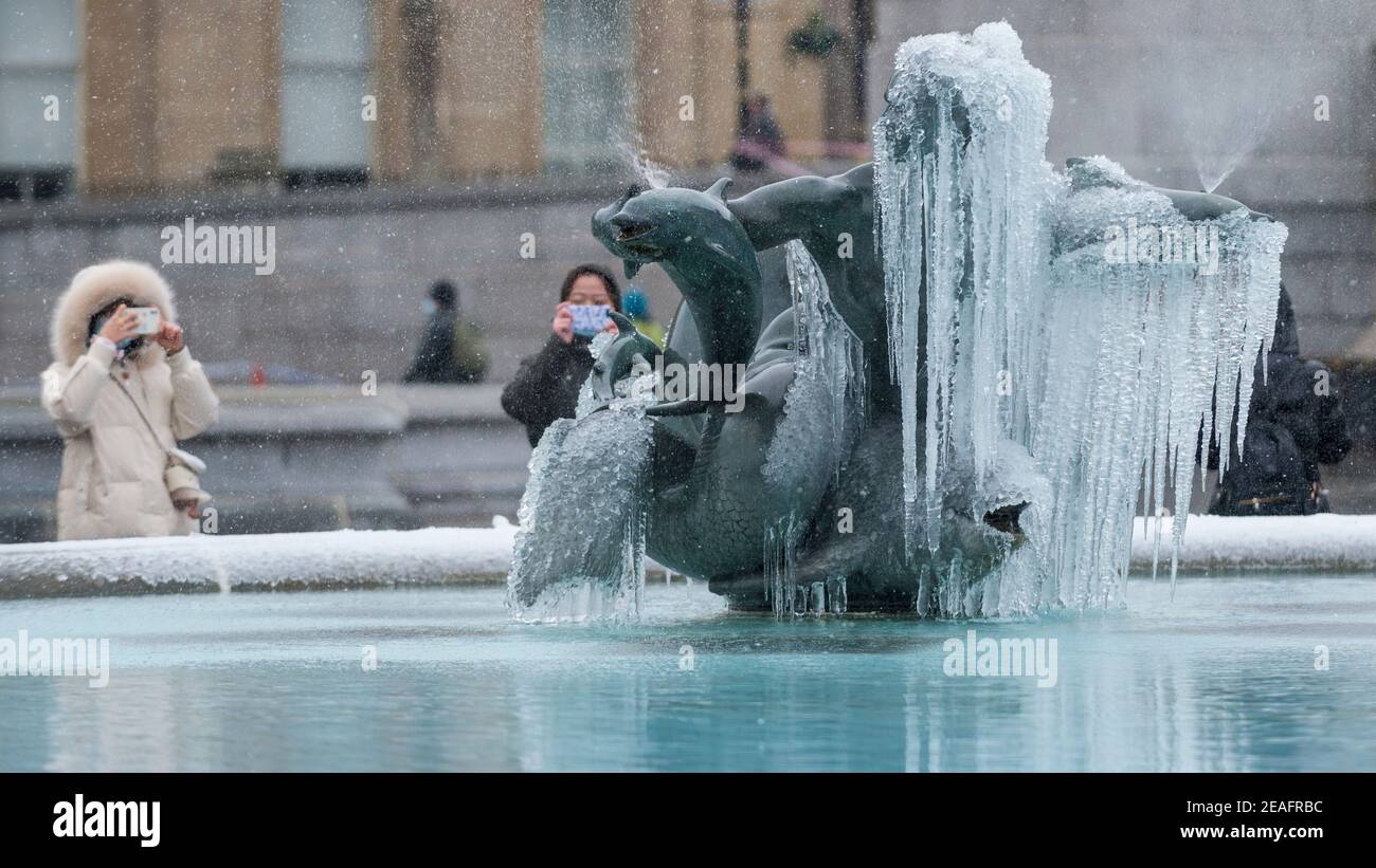 Londra, Regno Unito. 9 febbraio 2021. UK Weather: Le donne visualizzano una fontana ghiacciata coperta di ghiaccio in Trafalgar Square durante le nevi leggere come il freddo tempo portato da Storm Darcy continua. Credit: Stephen Chung / Alamy Live News Foto Stock