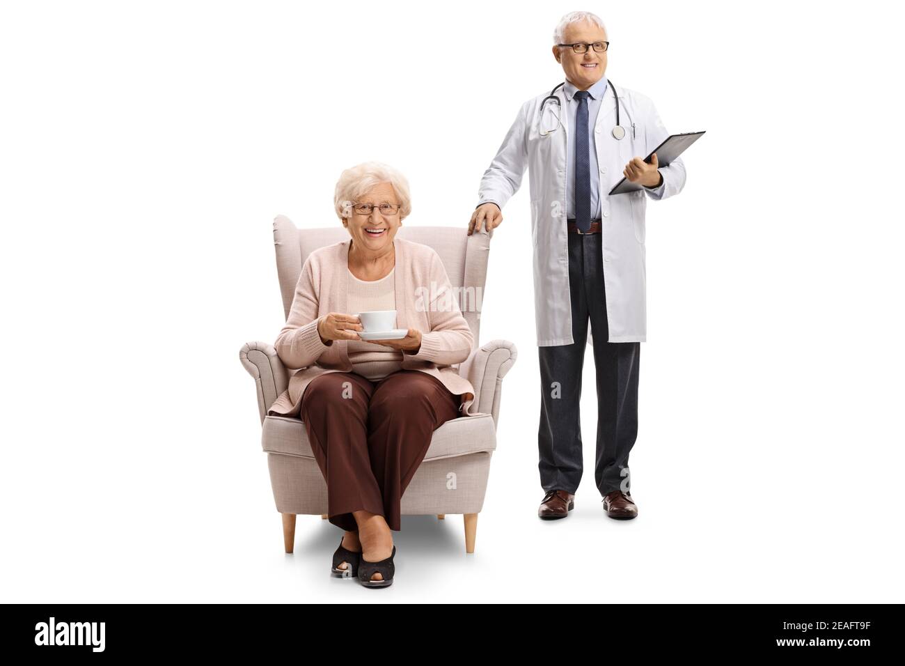 Medico maturo in piedi accanto ad una donna anziana in un poltrona con una tazza di tè isolato su sfondo bianco Foto Stock