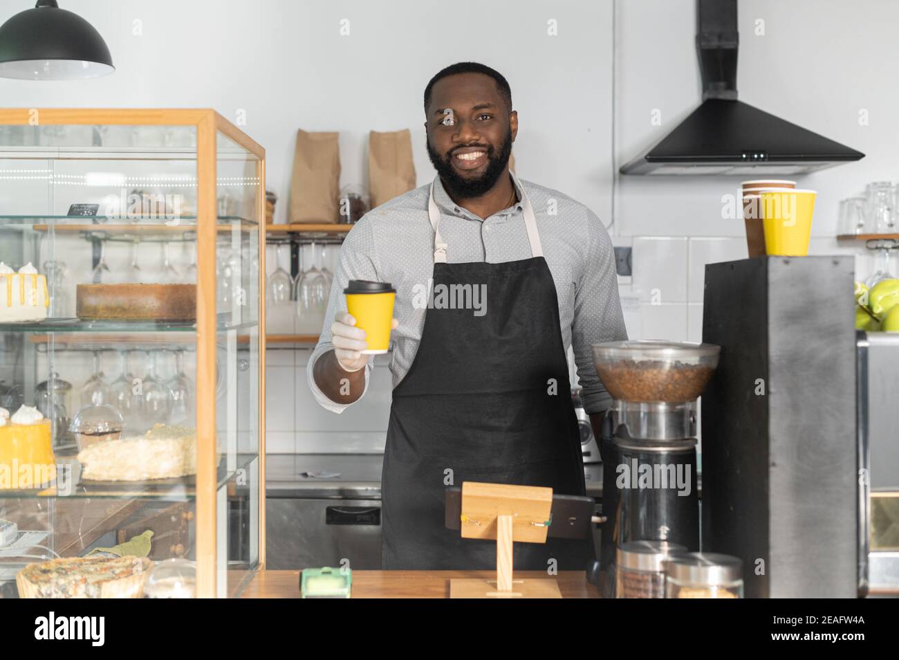 Un amichevole afroamericano cameriere che dà una tazza di caffè take away ordine, un barista multirazziale che indossa guanti e grembiule serve il cliente, guarda Foto Stock