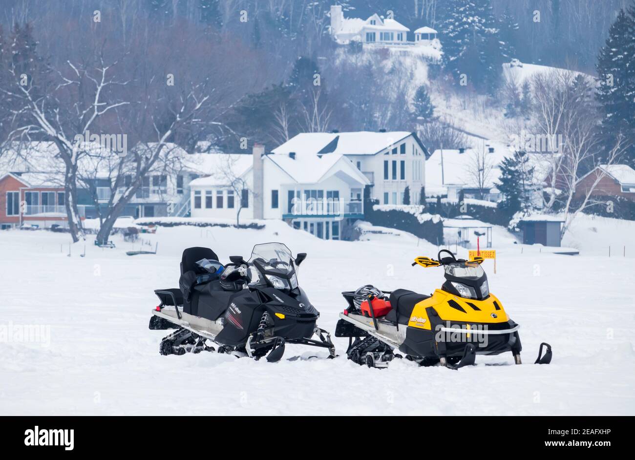 2 febbraio 2019- Grandes-Piles, QC, Canada: Due motoslitte parcheggiate su un lago ghiacciato e le case sullo sfondo, Mauricie Foto Stock