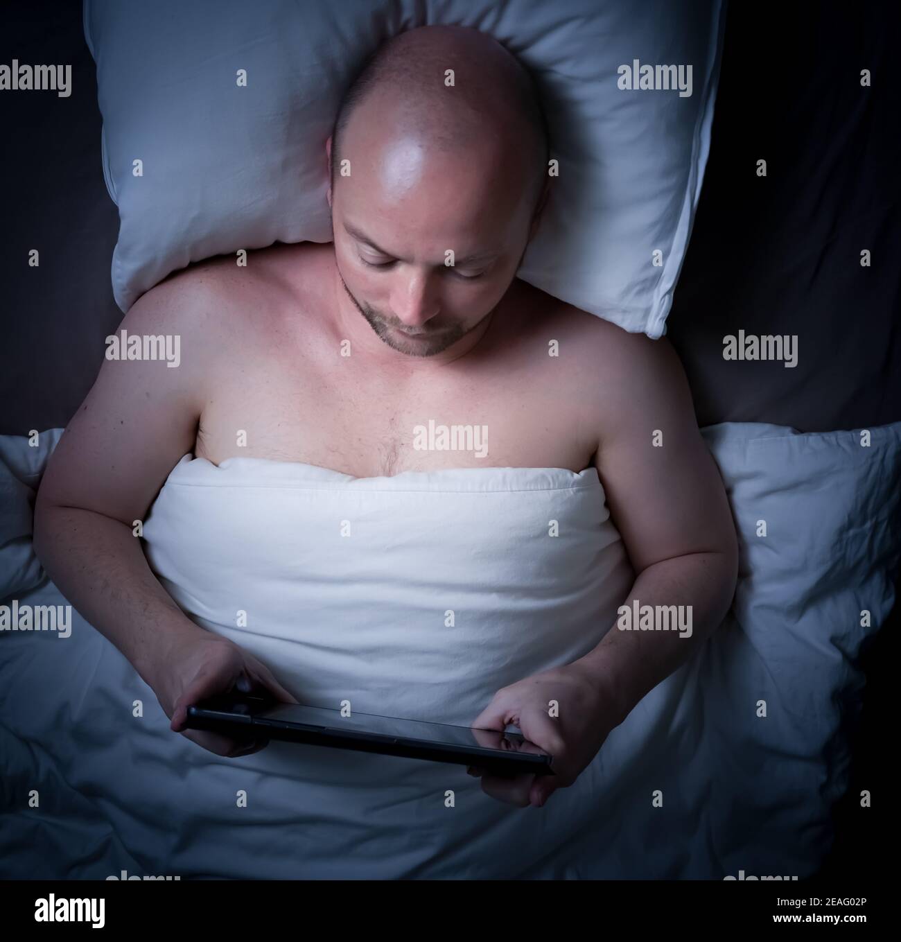Uomo sdraiato a letto di notte guardando il suo tablet. Foto Stock