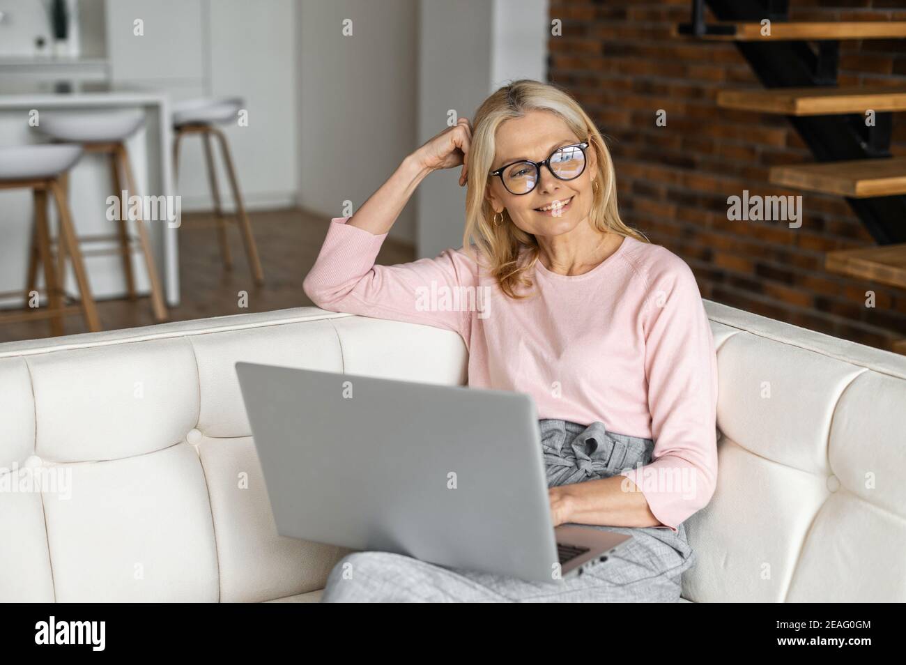 Bella donna bionda matura positiva in occhiali seduti sul divano,  riposandosi rilassante, pensando agli oggetti da acquistare, progettando di  guardare il film online Foto stock - Alamy