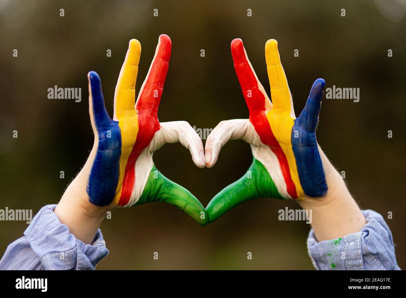 Mani di capretto dipinte in Seychelles bandiera colore mostra simbolo di il cuore e il gesto d'amore sullo sfondo della natura Foto Stock