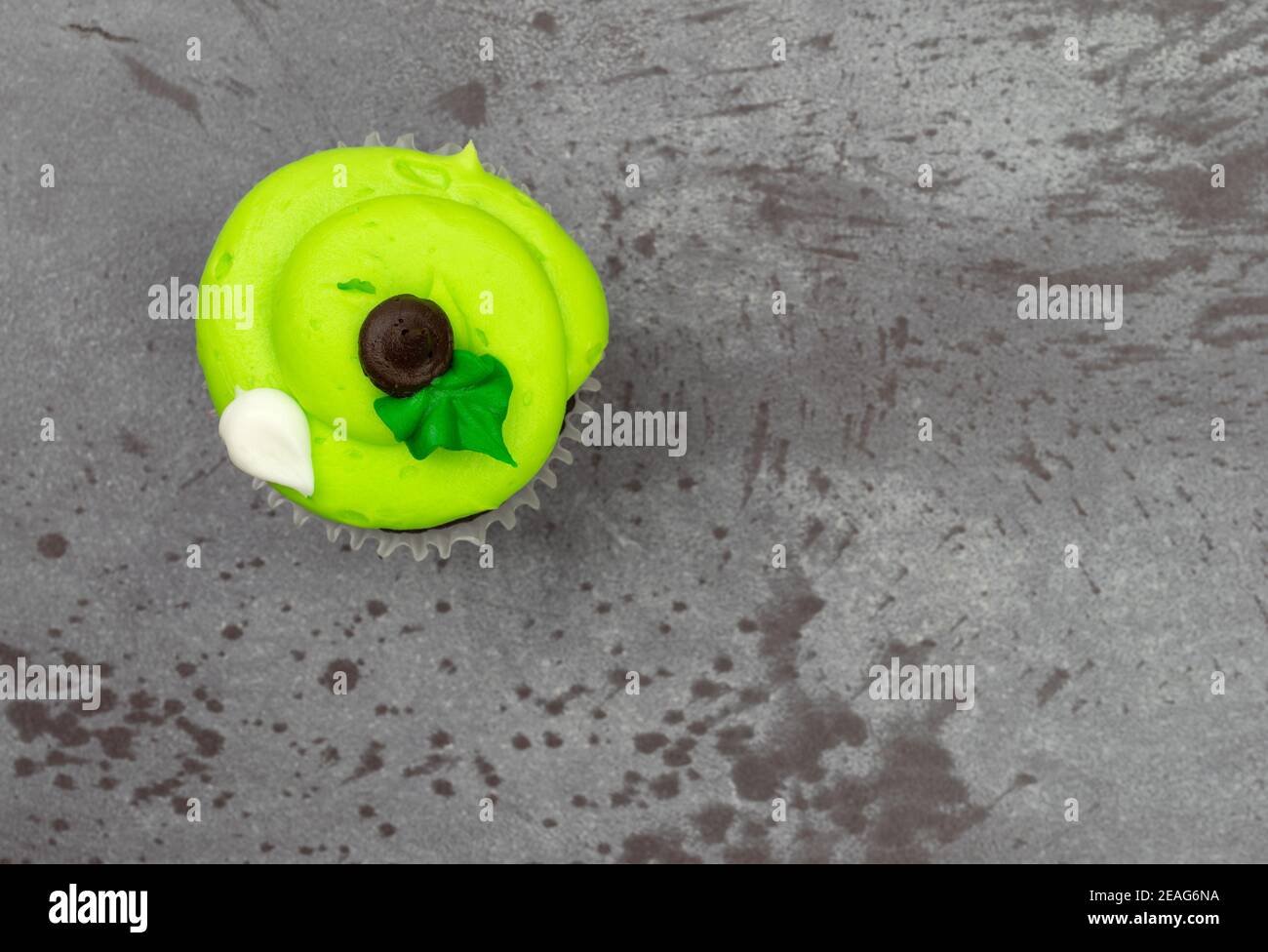 Vista dall'alto di un cupcake verde decorato con glassy glassed con accenti sfalsati su uno sfondo grigio. Foto Stock