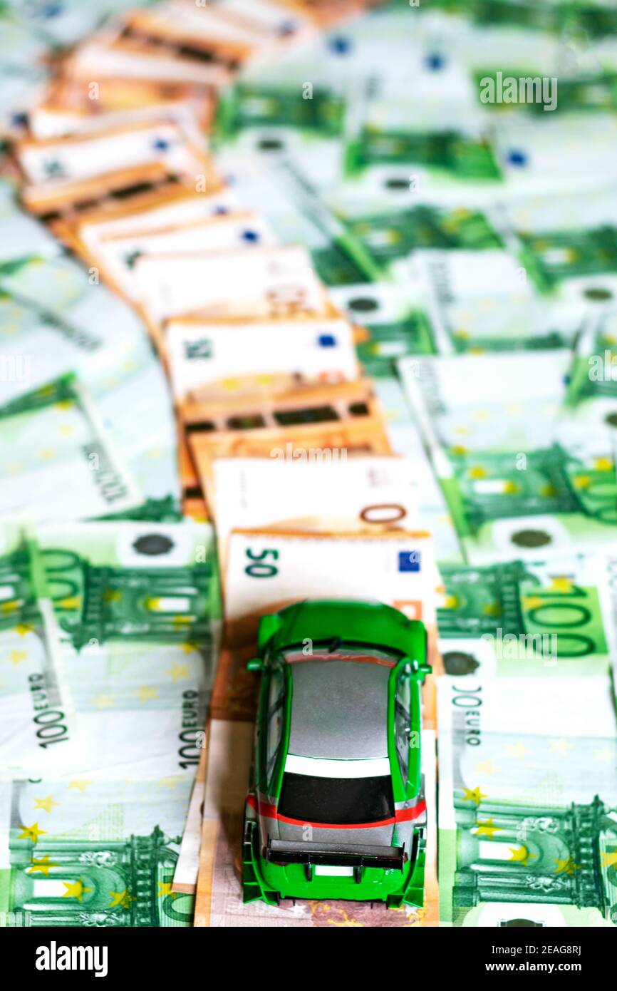 Macchinetta giocattolo su un percorso composto da cinquanta banconote da euro delimitate da banconote verdi da cento euro. Foto Stock