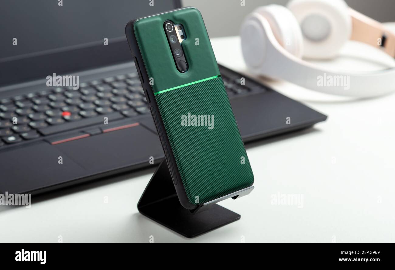 Smartphone sul supporto nella custodia protettiva sul retro dello smartphone vicino al computer portatile nero su un moderno spazio di lavoro bianco. Tavolo bianco a casa o in ufficio con telefono Foto Stock