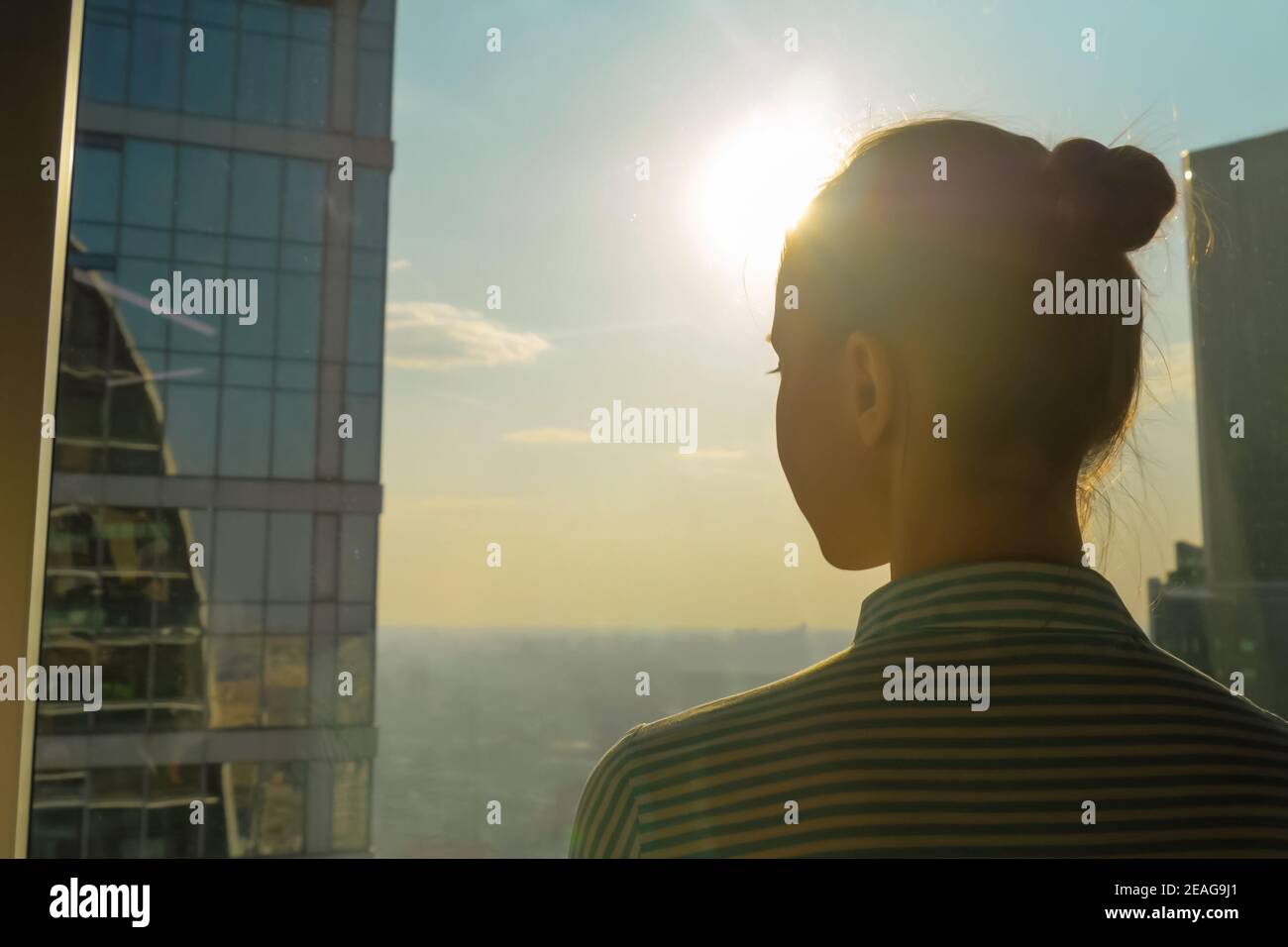 Vista posteriore della silhouette donna che guarda il paesaggio urbano attraverso la finestra di grattacieli Foto Stock