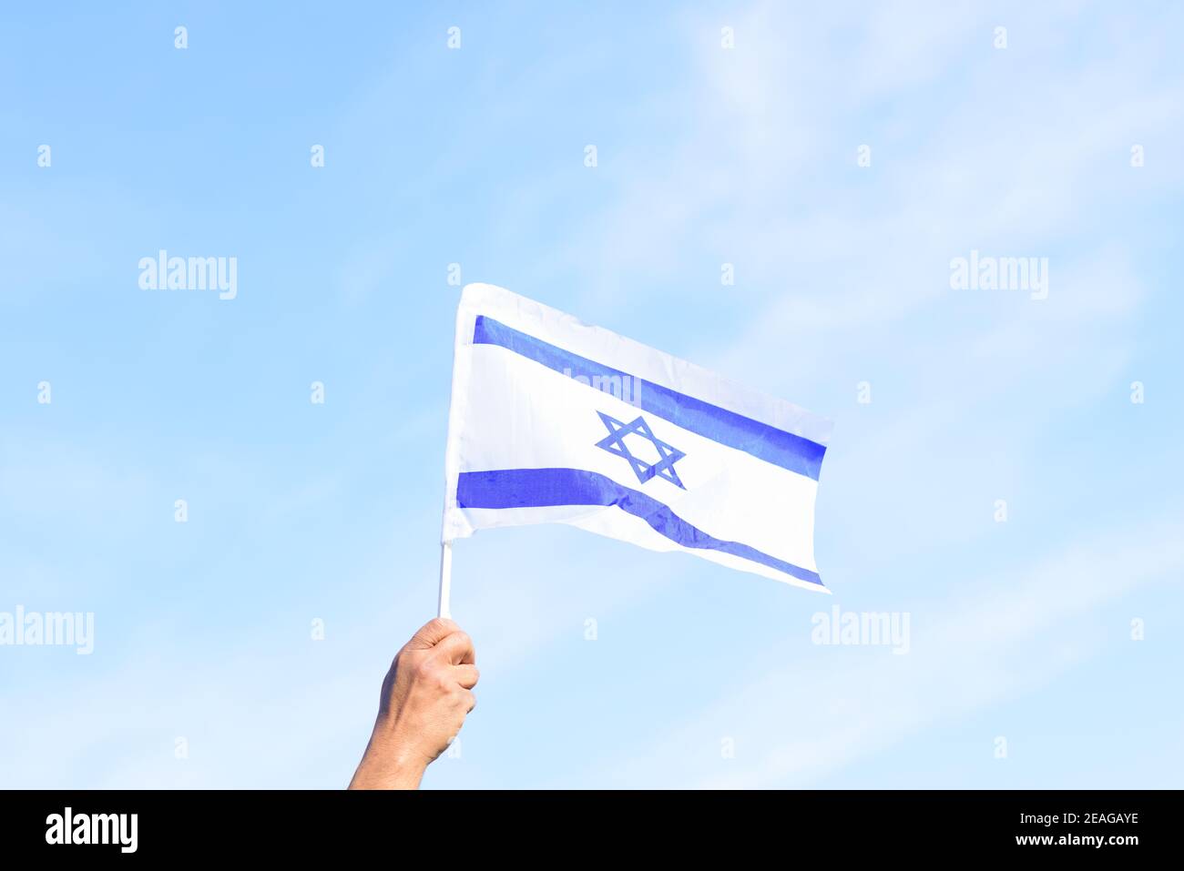Bandiera israeliana, mano dell'uomo, cielo blu, natura background.Memorial day-Yom Hazikaron, festa patriottica giorno di indipendenza Israele - Yom Ha'atzmaut concetto. Foto Stock