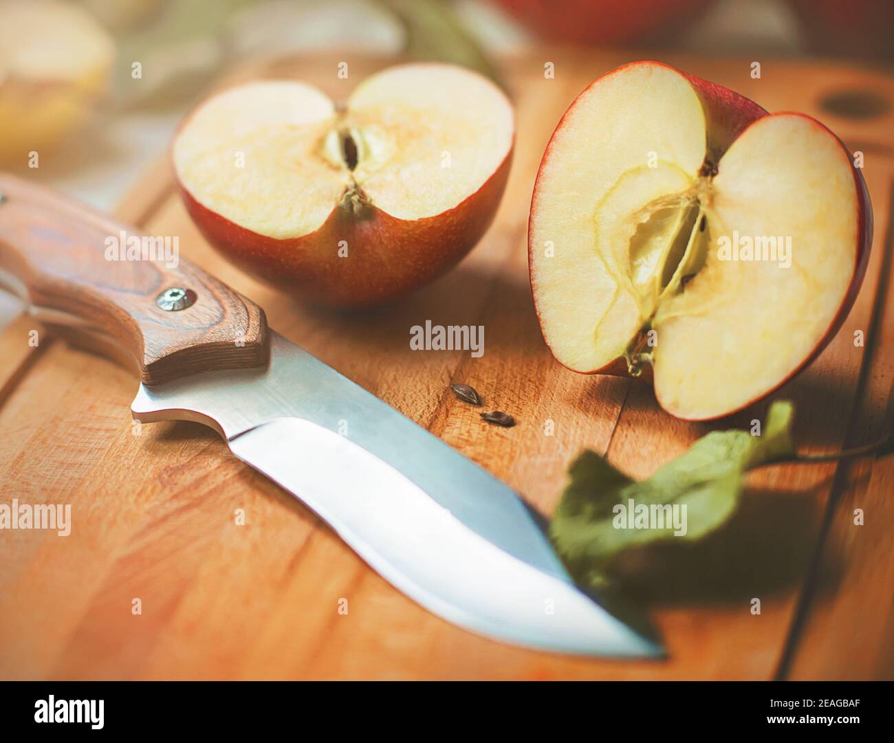 Una mela succosa rossa matura è stata tagliata con un coltello affilato e le sue metà giacciono su una tavola da cucina in legno, illuminata alla luce del sole in una giornata estiva. Har Foto Stock