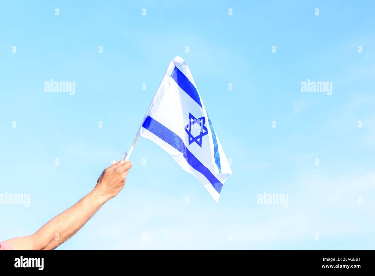 Bandiera israeliana, mano dell'uomo, cielo blu. Memoriale giorno-Yom Hazikaron, giorno di indipendenza Israele-Yom ha atzmaut concetto. Foto Stock