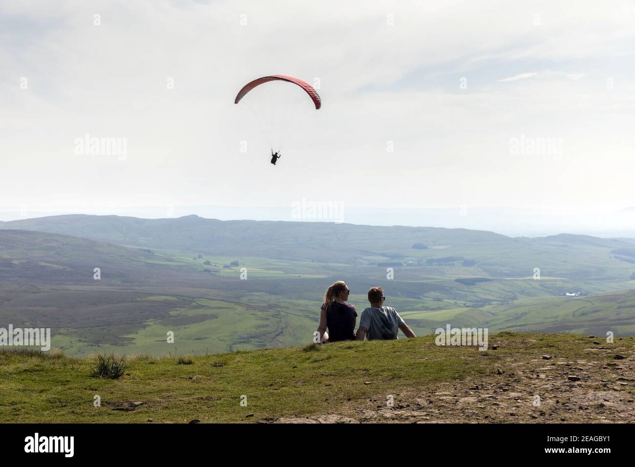 Una coppia siede sulla cima di Pen-y-gand nel Yorkshire Dales come parapendio vola passato Foto Stock