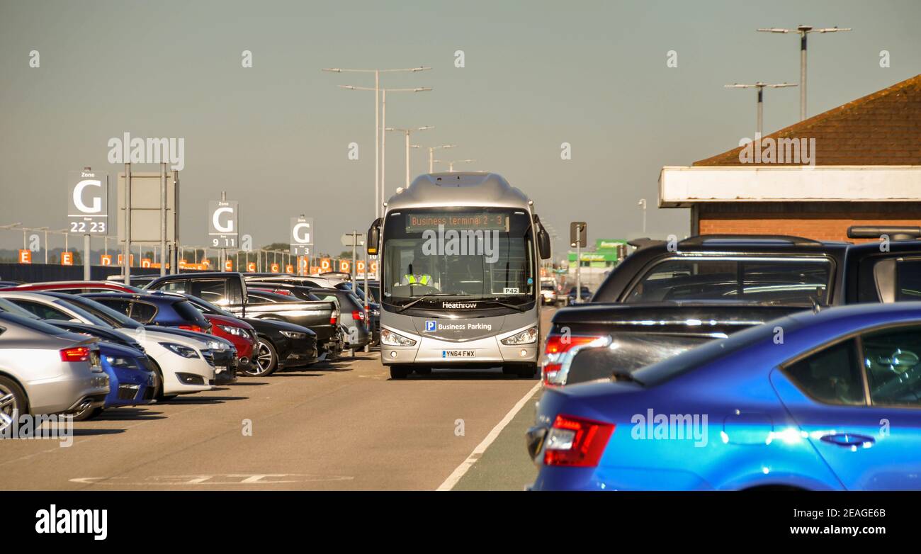 Londra, Inghilterra - Agosto 2018: Autobus navetta che guida tra file di auto parcheggiate in un parcheggio d'affari dell'aeroporto. Foto Stock