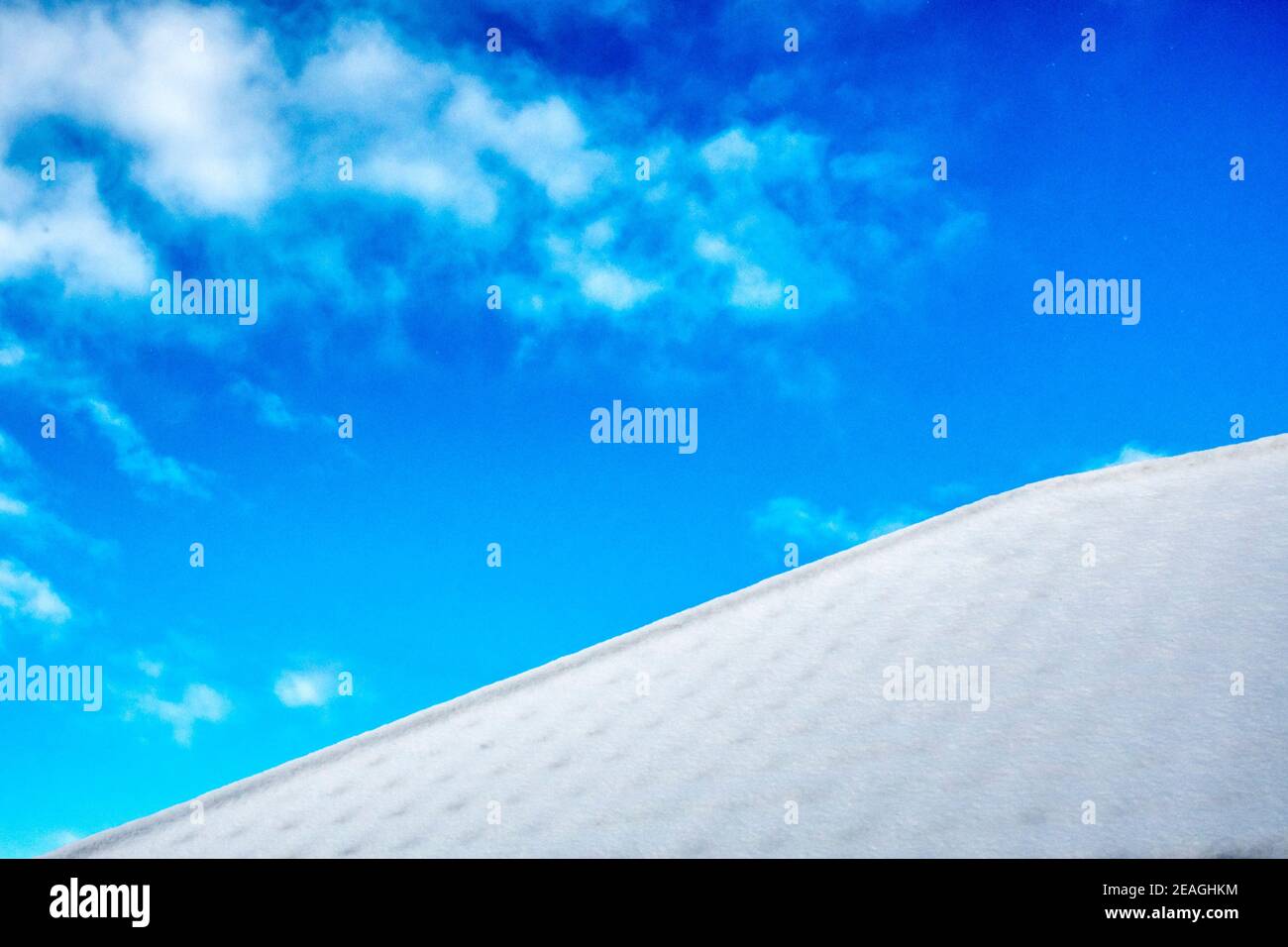 Neve bianca su un tetto visto contro un cielo blu luminoso. Foto Stock
