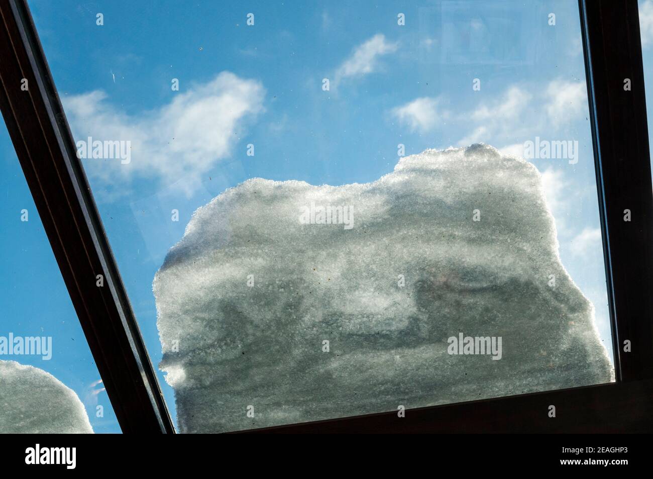 Neve sul tetto di vetro di una serra isolata con doppi vetri, vista dall'interno. Contro un cielo blu. Foto Stock