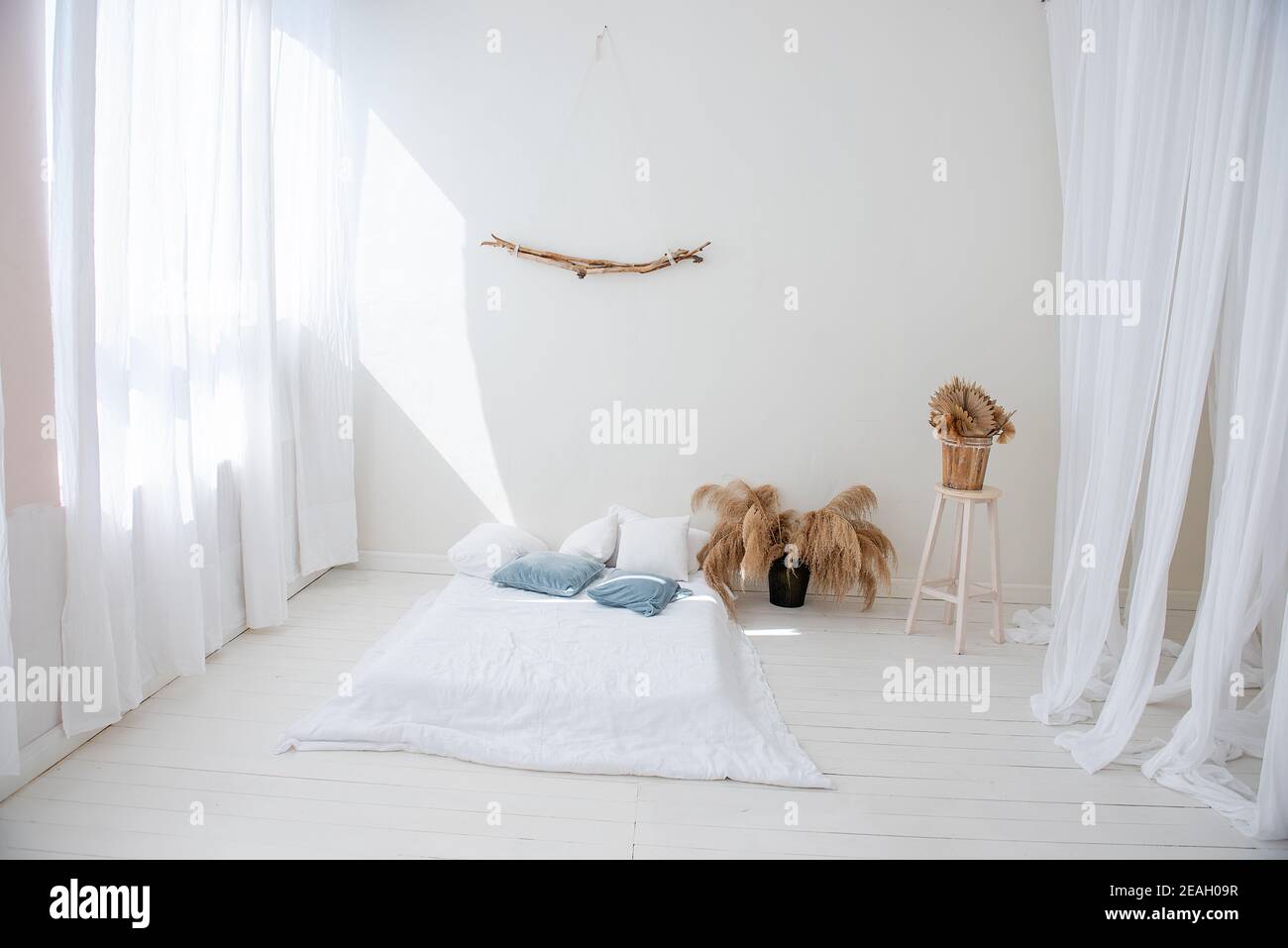 Loft bianco minimalista in stile scandinavo. C'è letto su pavimento in legno, tulles arioso chiaro sulle finestre, vi è pampas erba in vasi Foto Stock