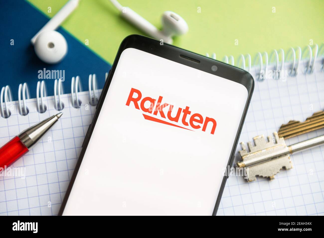 In questa illustrazione fotografica, viene visualizzato un logo Rakuten su uno smartphone con una penna, una chiave, un libro e un auricolare sullo sfondo. Foto Stock
