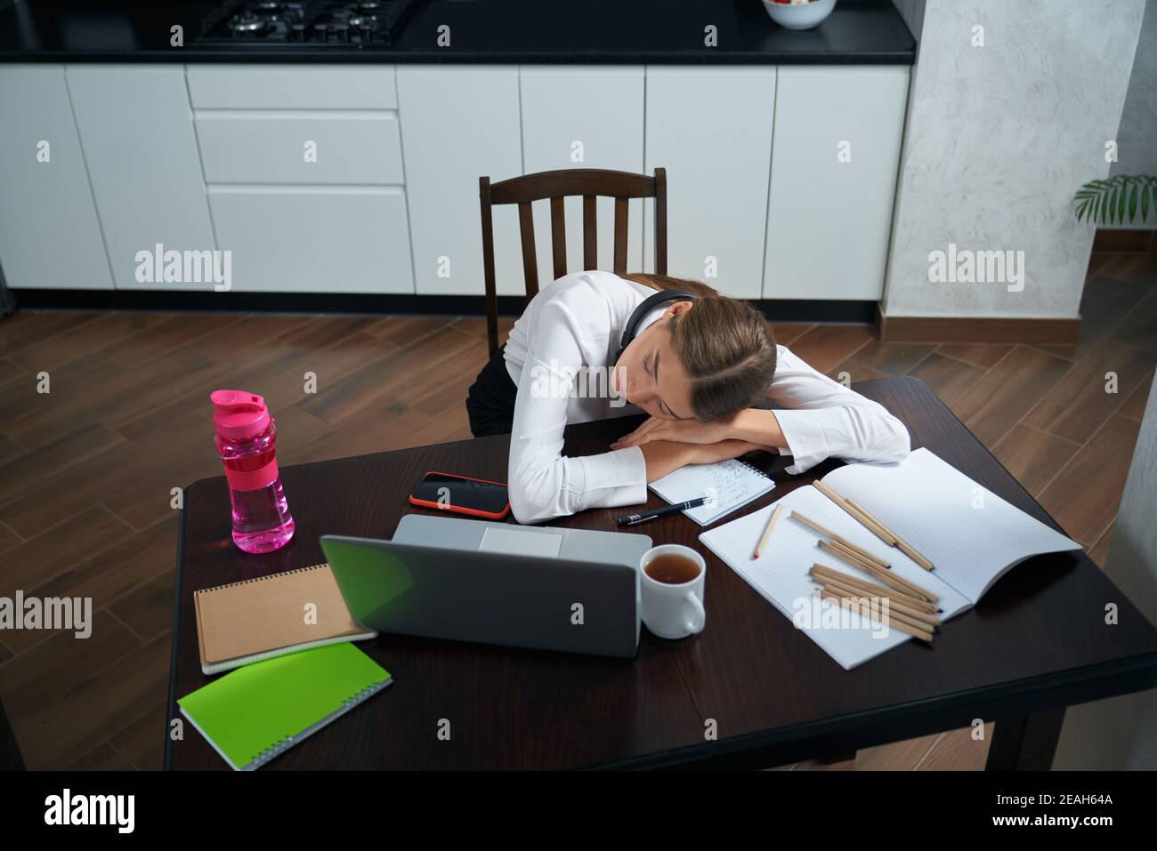 Stanca giovane donna che dorme al tavolo dopo una lunga giornata di lavoro a casa. Donna che utilizza un computer portatile e uno smartphone moderni. Concetto di persone e lavoro eccessivo. Foto Stock