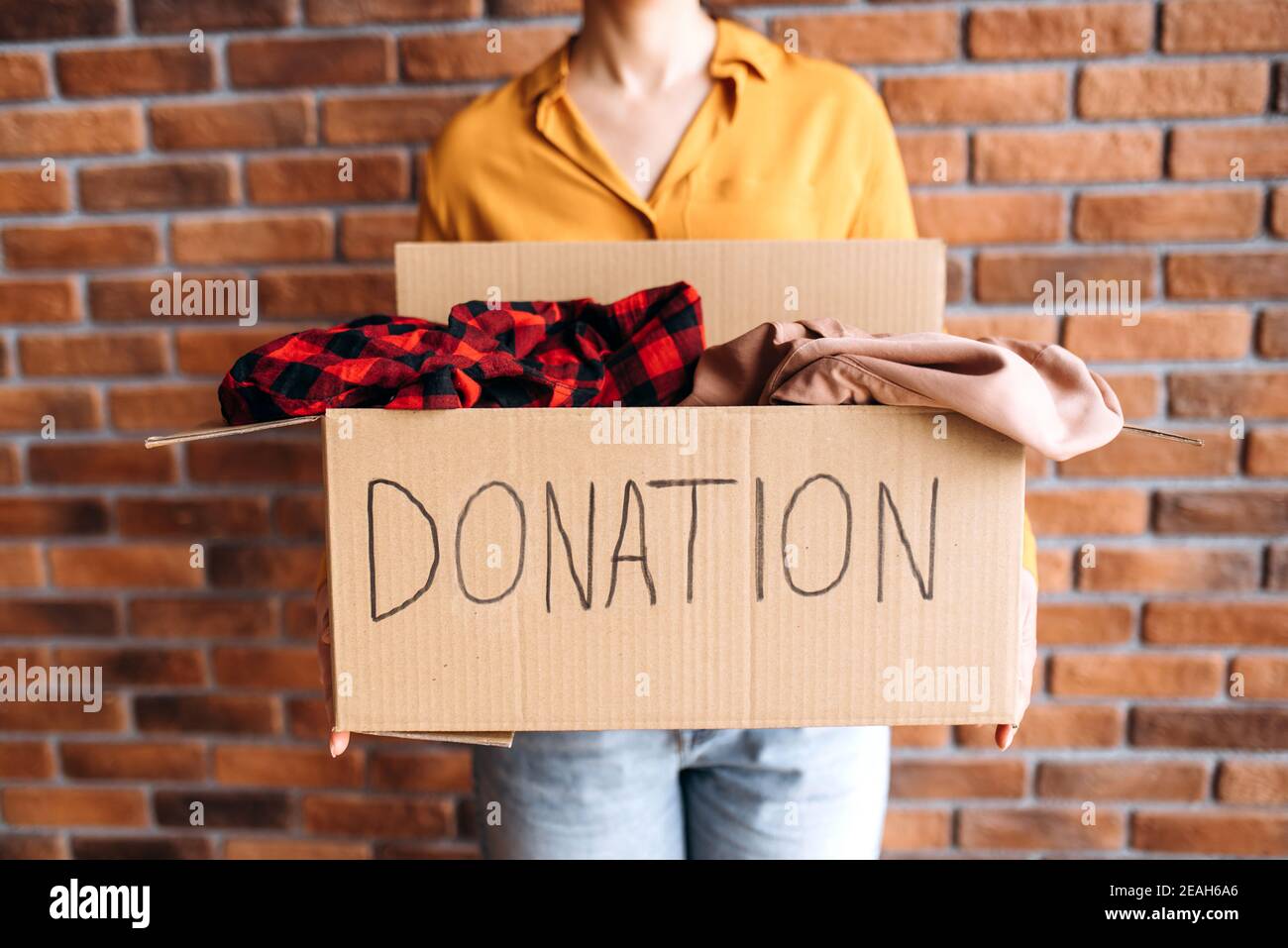 Concetto di donazione. Donna che tiene una scatola di donate con i vestiti pieni, per il riutilizzo o il riciclaggio di vecchi vestiti. Carità. Aiutare le persone povere e bisognose Foto Stock