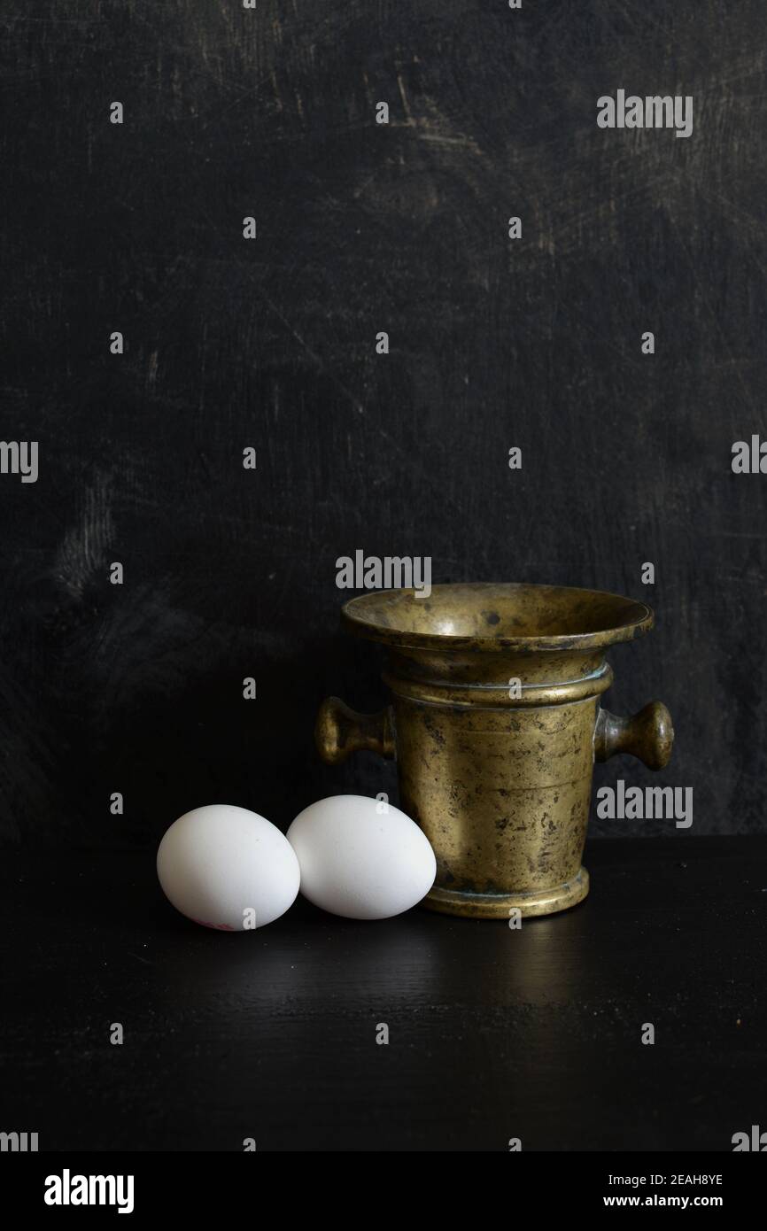 Antico mortaio di ottone e due uova bianche Foto Stock