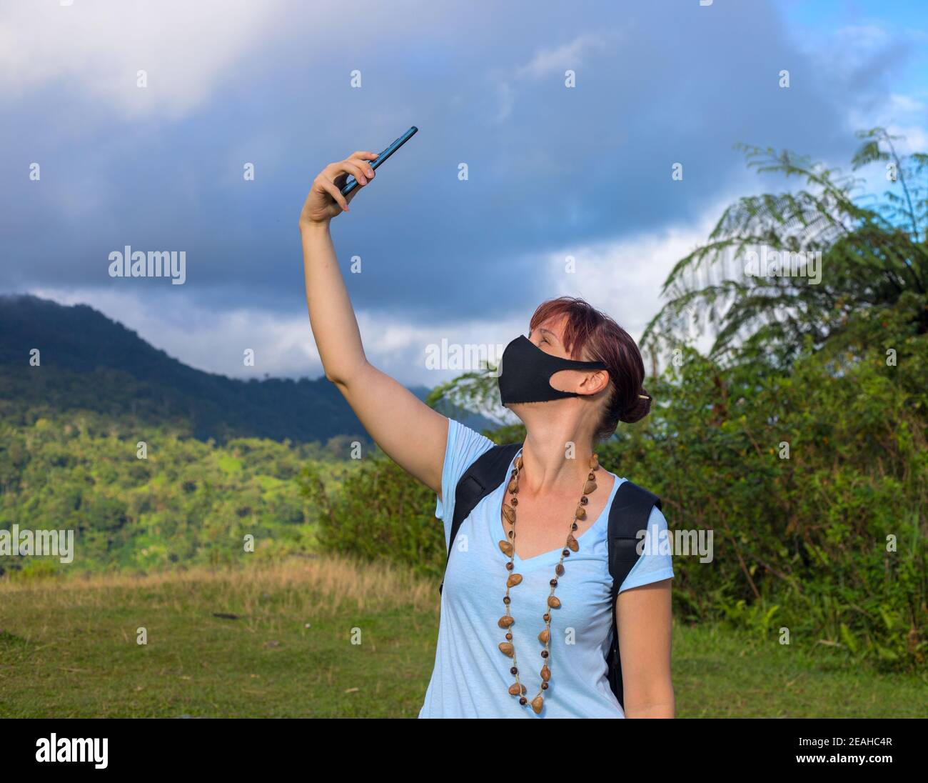 Una donna mascherata che cerca di trovare un segnale del telefono cellulare. Ricerca di connessione mobile in natura selvaggia in vacanza. Perfetto giorno all'aperto. Nessuna comunicazione o Foto Stock