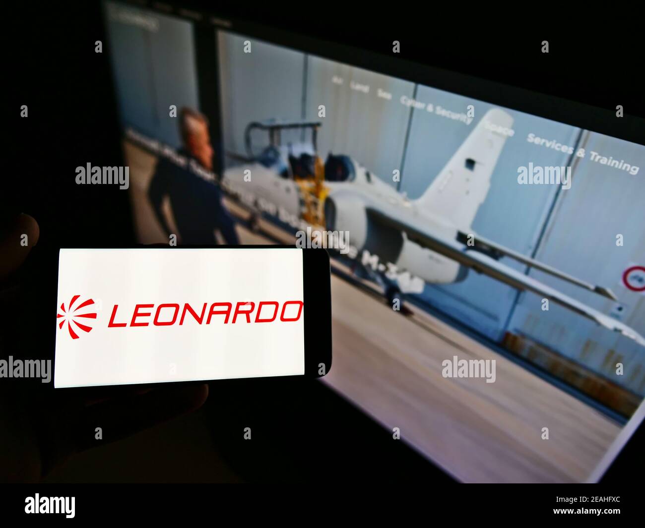 Persona titolare di un telefono cellulare con logo della società italiana di difesa Leonardo S.p.A. sullo schermo davanti alla pagina web aziendale. Focus sul display del cellulare. Foto Stock