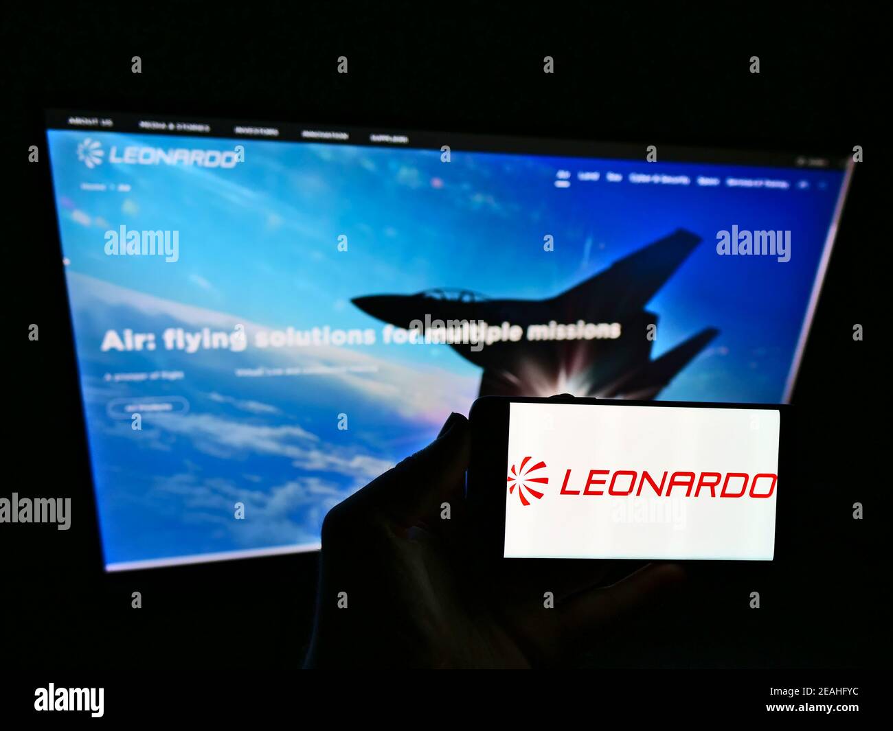 Persona titolare del cellulare con logo della società italiana di aerospazio e difesa Leonardo S.p.A. sullo schermo davanti alla pagina web. Mettere a fuoco il display del telefono. Foto Stock