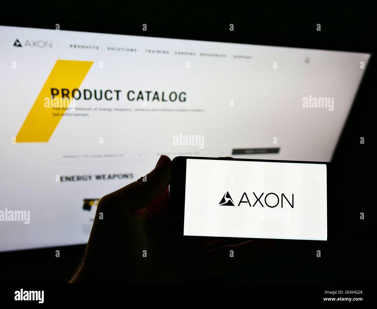 Persona che tiene il telefono cellulare con il logo del produttore americano di armi Axon Enterprise Inc. Sullo schermo davanti alla pagina web. Focus sul display del cellulare. Foto Stock