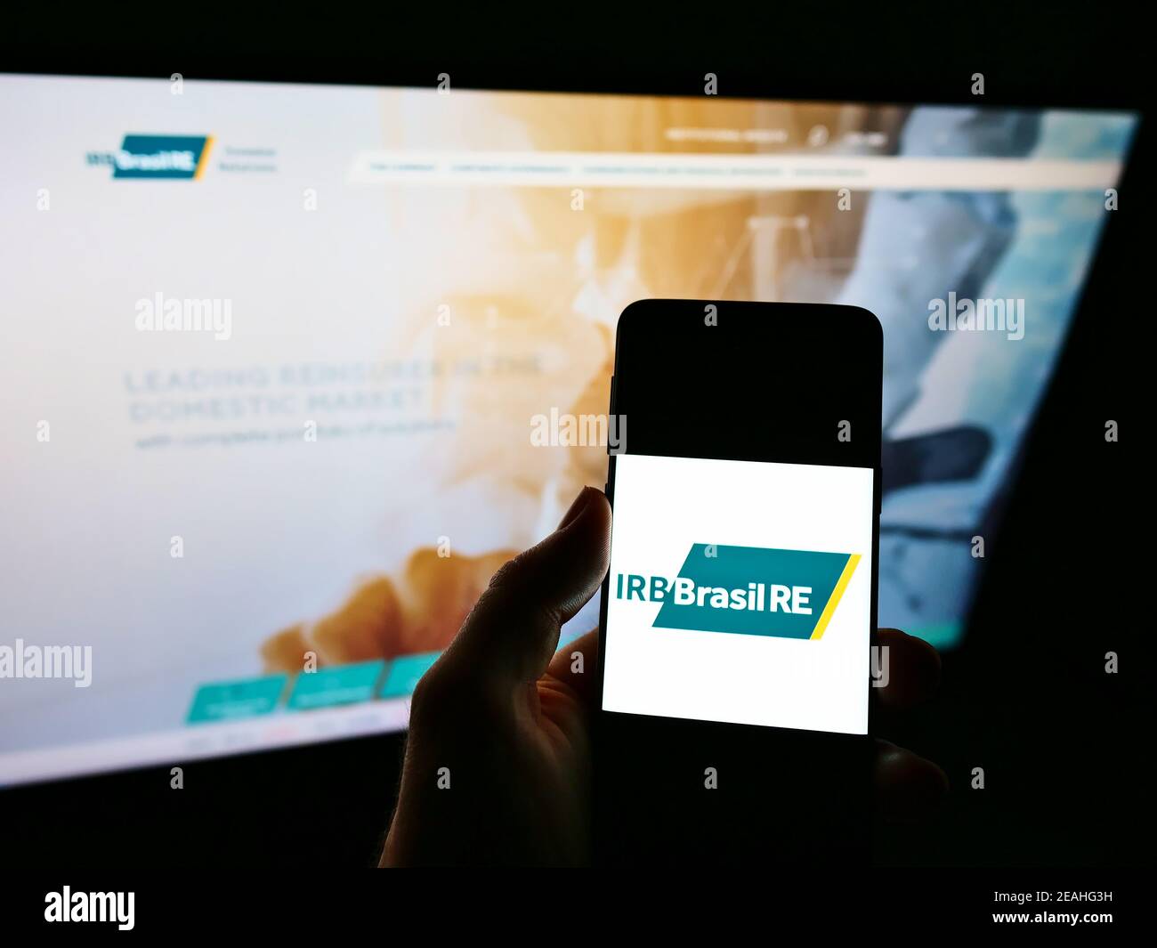 Persona che detiene il telefono cellulare con il logo della compagnia di riassicurazione IRB Brasil RE sullo schermo davanti al sito web aziendale. Focus sul display del cellulare. Foto Stock