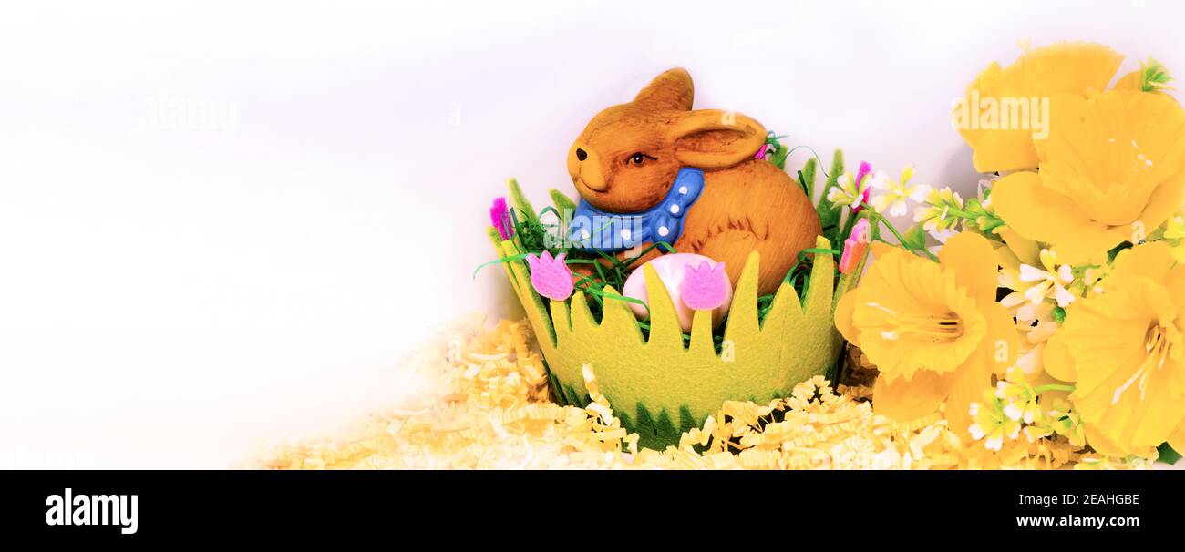 Coniglietto pasquale con uova in un cesto pasquale verde su sfondo bianco, decorazione floreale e spazio per il testo Foto Stock