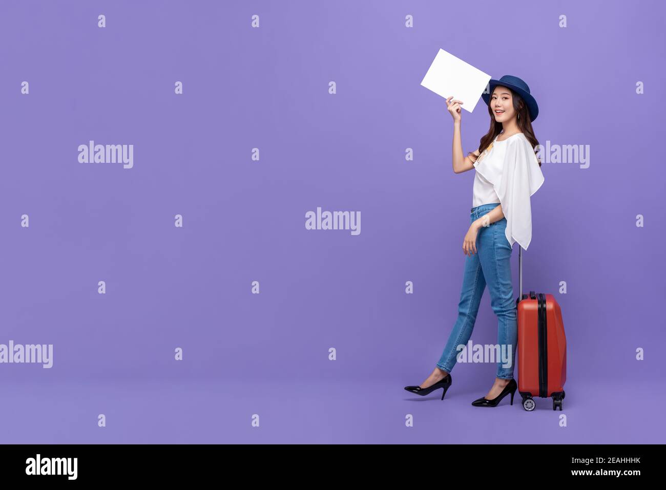 Giovane bella donna turistica asiatica con bagaglio in bianco carta isolata su sfondo viola dello studio con spazio per la copia Foto Stock