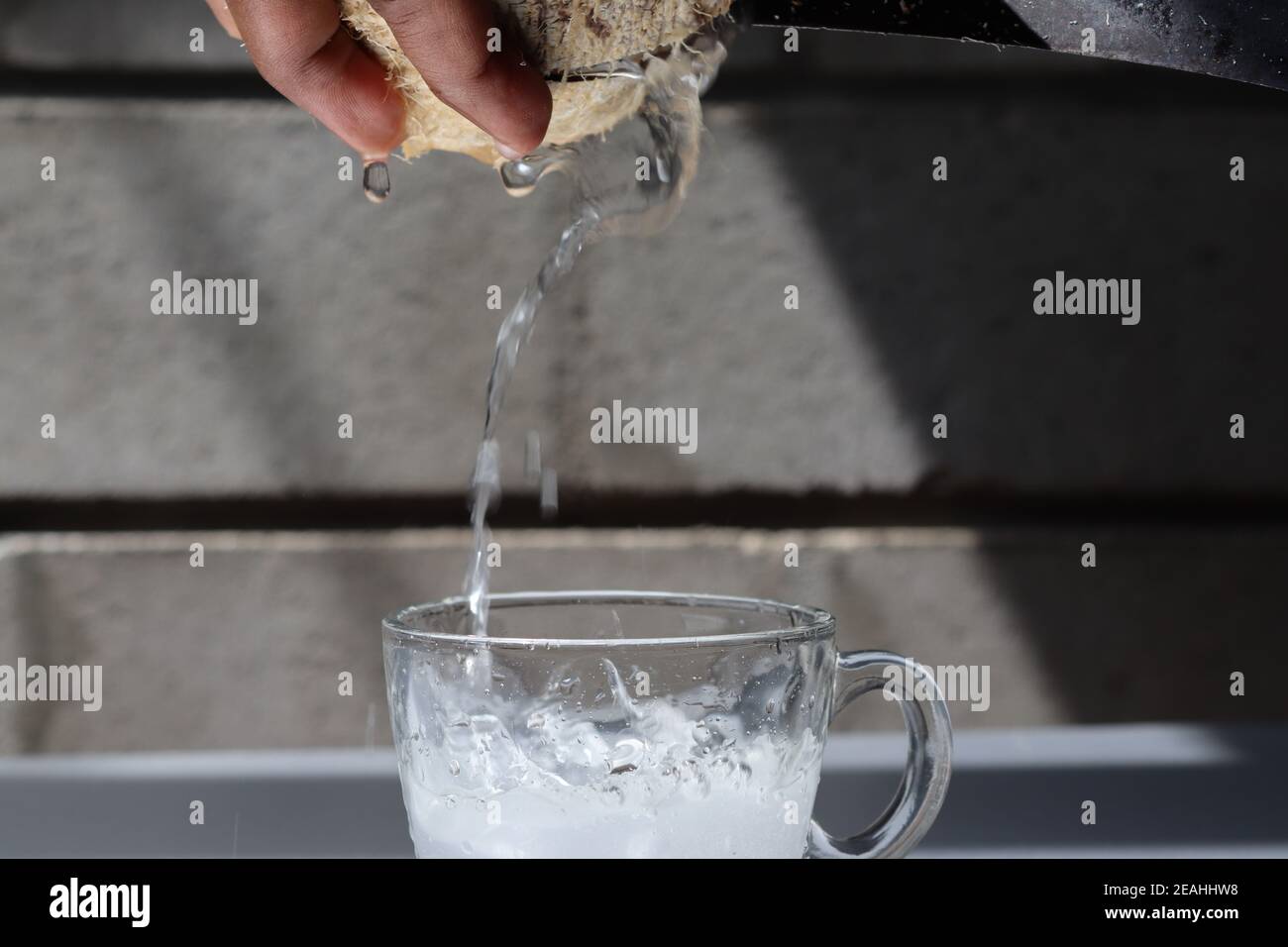 Quando si rompe un cocco, acqua di cocco molto gustosa che si versa in una tazza di vetro. Questa acqua di cocco è una bevanda forte e sana dalla natura. Molto gustoso. Foto Stock