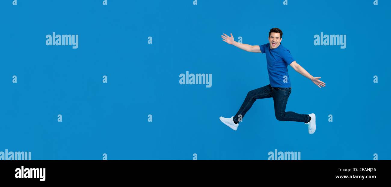 Energico giovane bell'uomo che salta e sorride con mani distese isolato in sfondo blu banner con spazio di copia Foto Stock