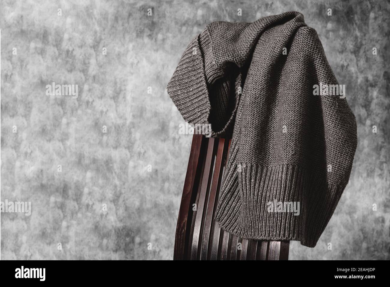 Maglia grigia sul retro della sedia in legno contro parete grigia in cemento. Stile minimalista. Spazio di copia Foto Stock