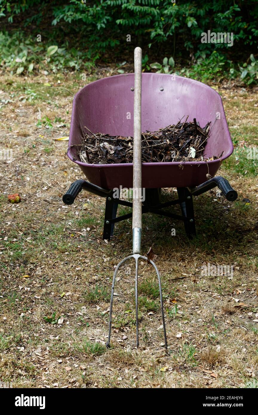 Compost in un carriola rosso o borgogna, ha una forchetta che pende contro di esso Foto Stock