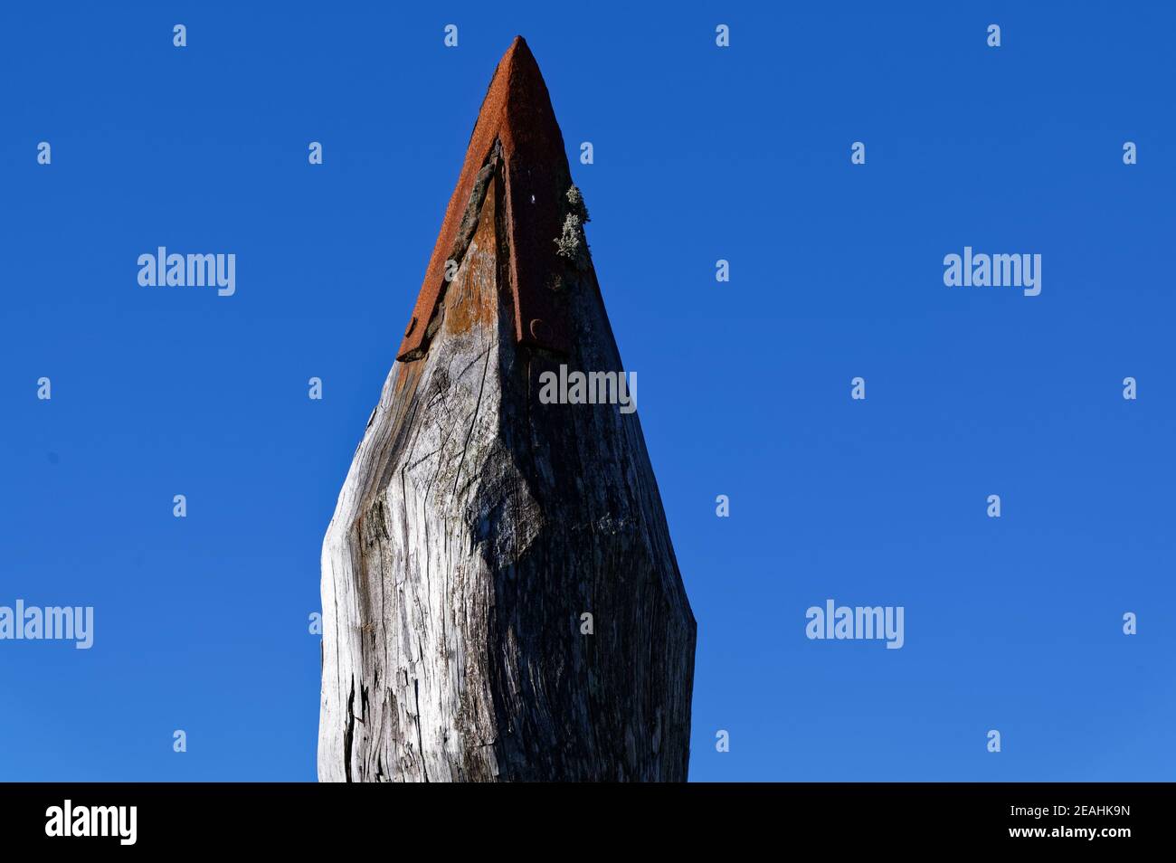 Un palo di legno è coperto di metallo arrugginito, sembra una grande matita, sta raggiungendo il cielo blu. Foto Stock