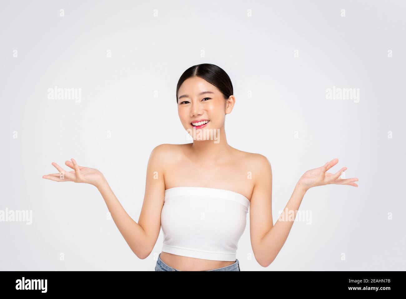 Beauty shot di giovane ragazza asiatica con pelle faccia incandescente sorridendo e aprendo mani vuote su sfondo bianco Foto Stock