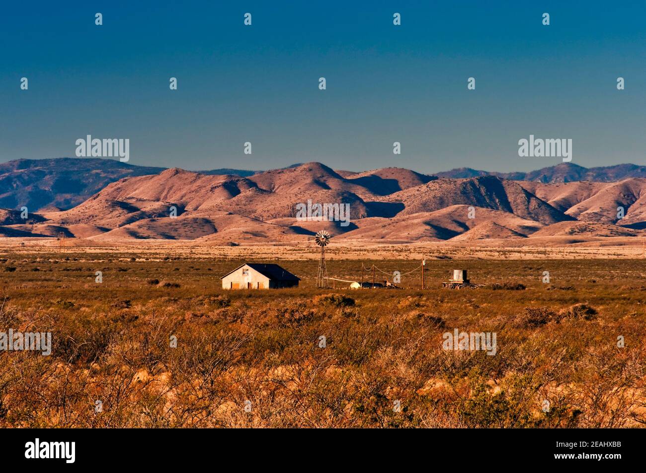 Ranch edificio, mulino a vento, Sierra Cuchillo in distanza, vista vicino Geronimo Trail, vicino Cuchillo, New Mexico, Stati Uniti Foto Stock