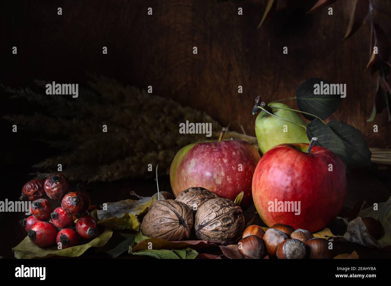 noci e frutta con fogliame in stile rustico al buio sfondo di legno Foto Stock