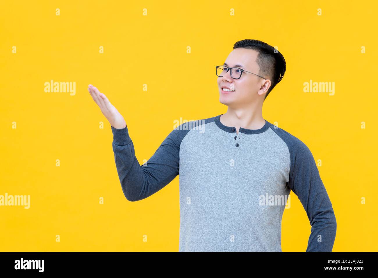 Amico giovane uomo asiatico intelligente che presenta gesto con la mano si apre su uno spazio vuoto isolato su sfondo giallo dello studio Foto Stock